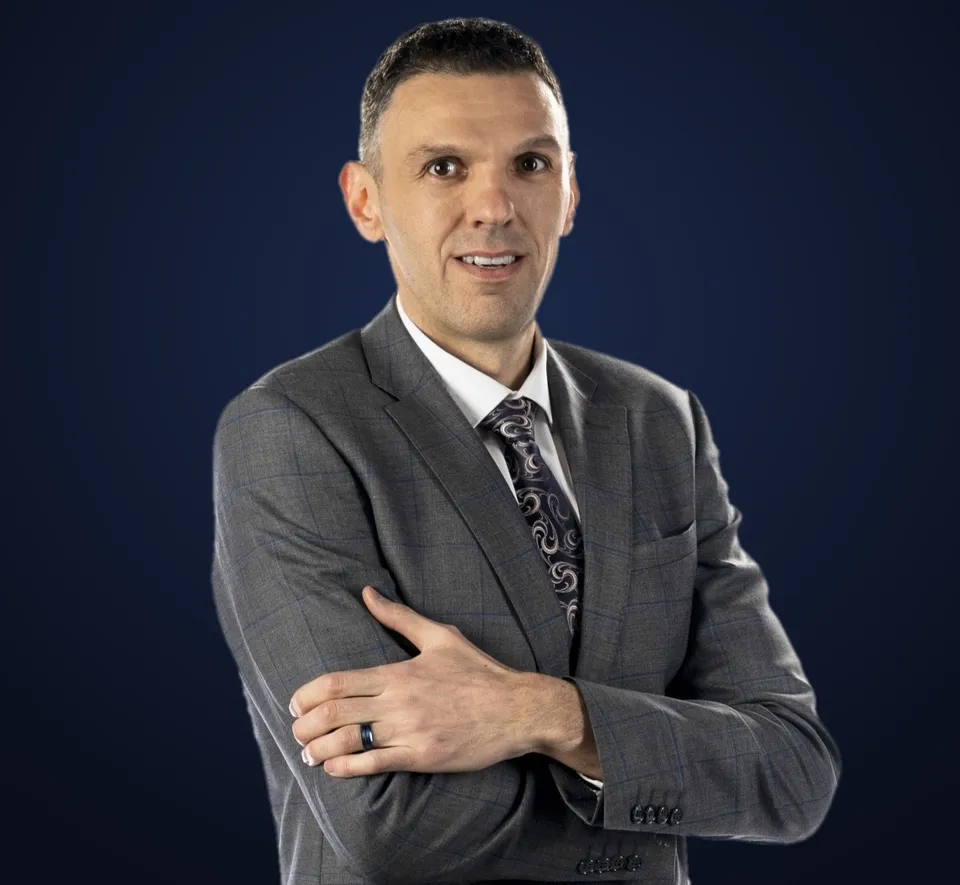 Lubo Bali in a gray suit, arms crossed, smiling